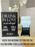 May include: A black rectangular bar sign with white text reading DRUNK IN LOVE we be all night MR. MARGARITA ON THE ROCKS MRS. EXPRESSO MARTINI The Grants, alongside a black square holder containing white heart-shaped drink stirrers labelled C+D.