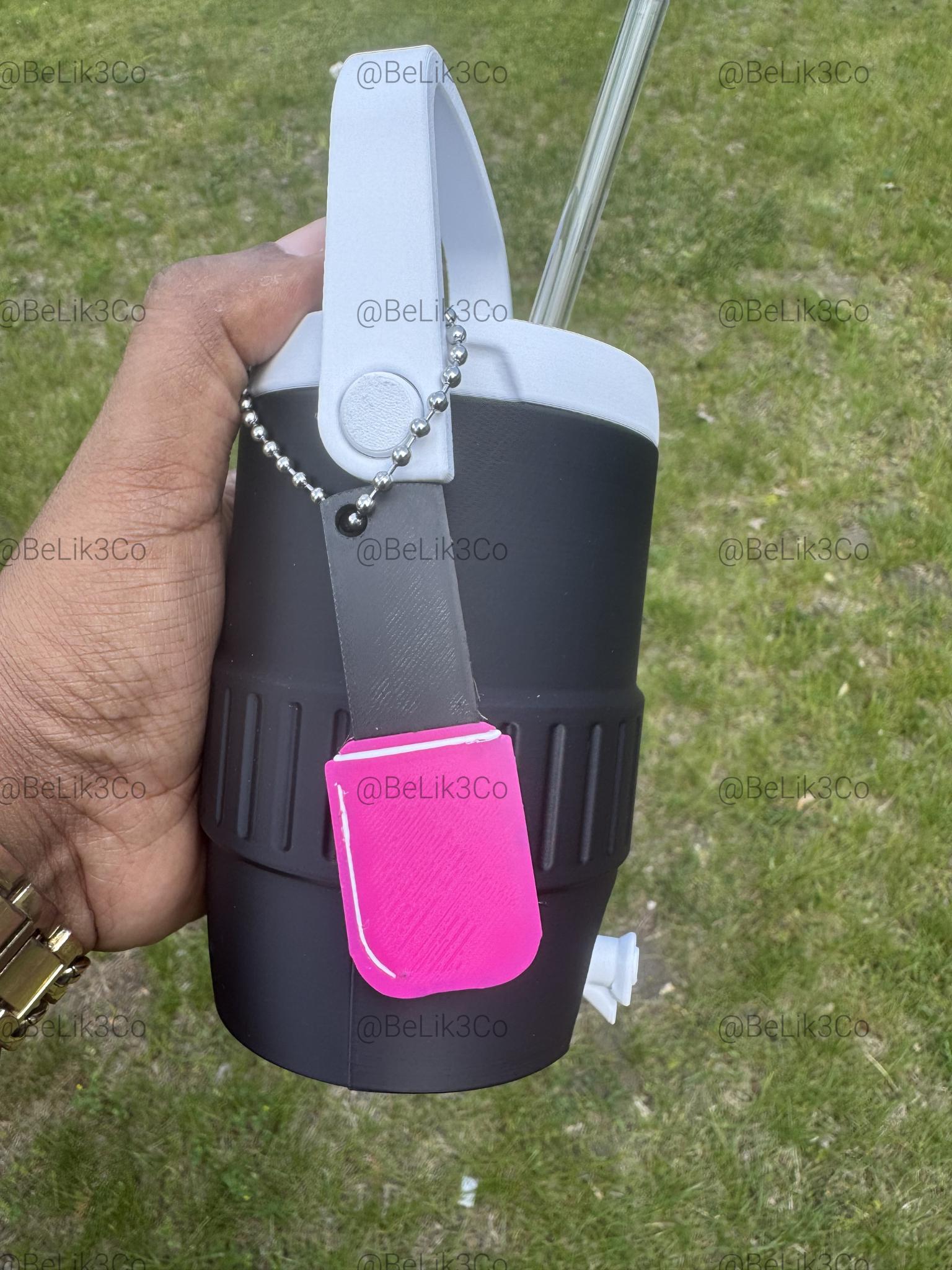 May include: A black insulated tumbler with a white handle and a clear straw. A grey rectangular tag with a bright pink rectangular attachment hangs from the handle by a silver ball chain. The text @BeLik3Co is repeated across the image.